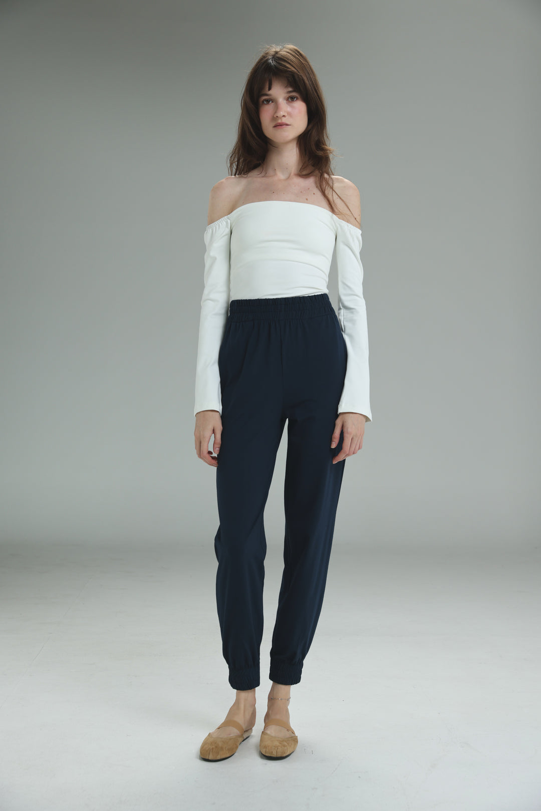 The lycra white off shoulder top with long sleeves is shown front view paired with dark navy high-waisted trousers