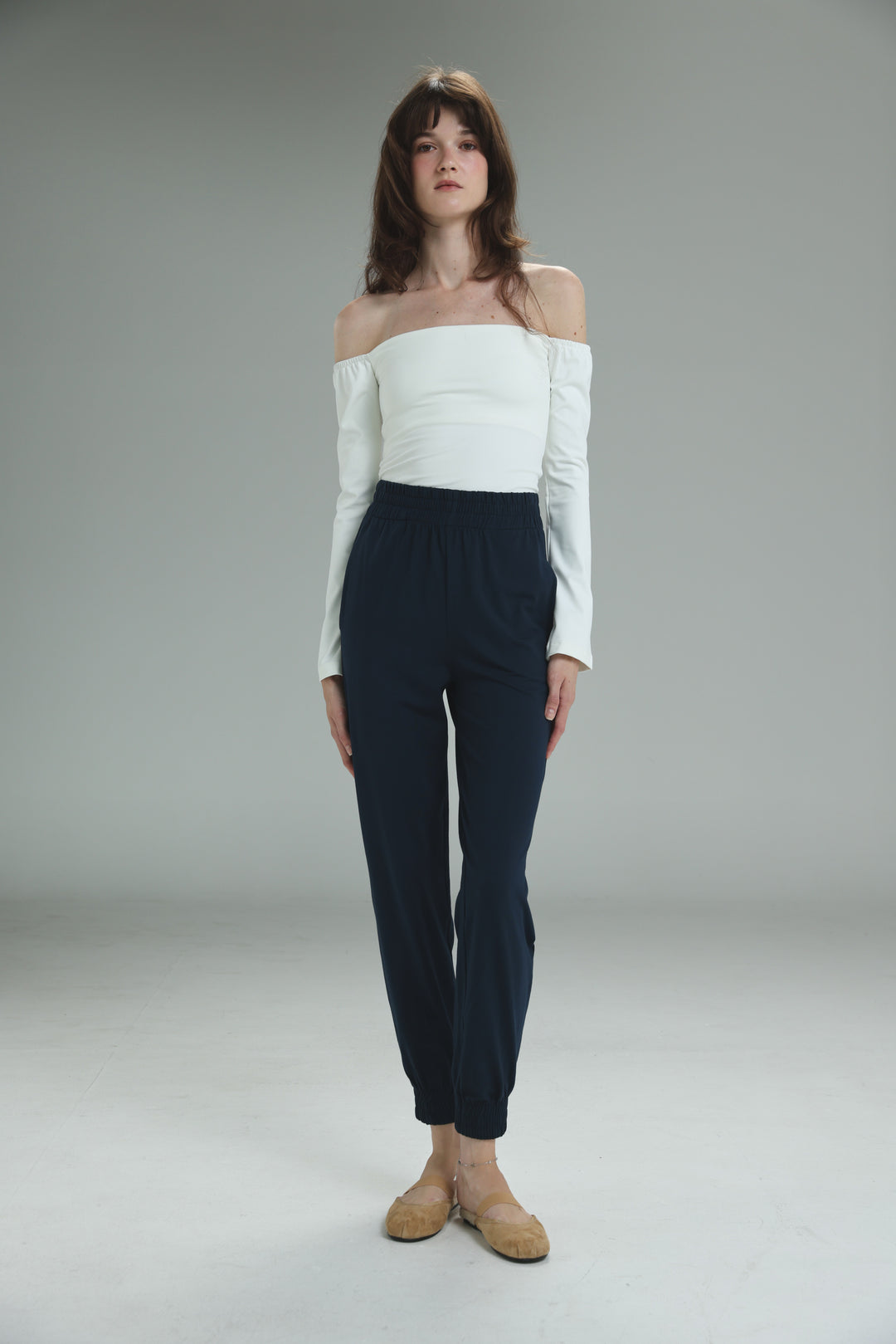 A woman wearing dark navy high-waisted Bestie joggers with a white off-the-shoulder top in a front view