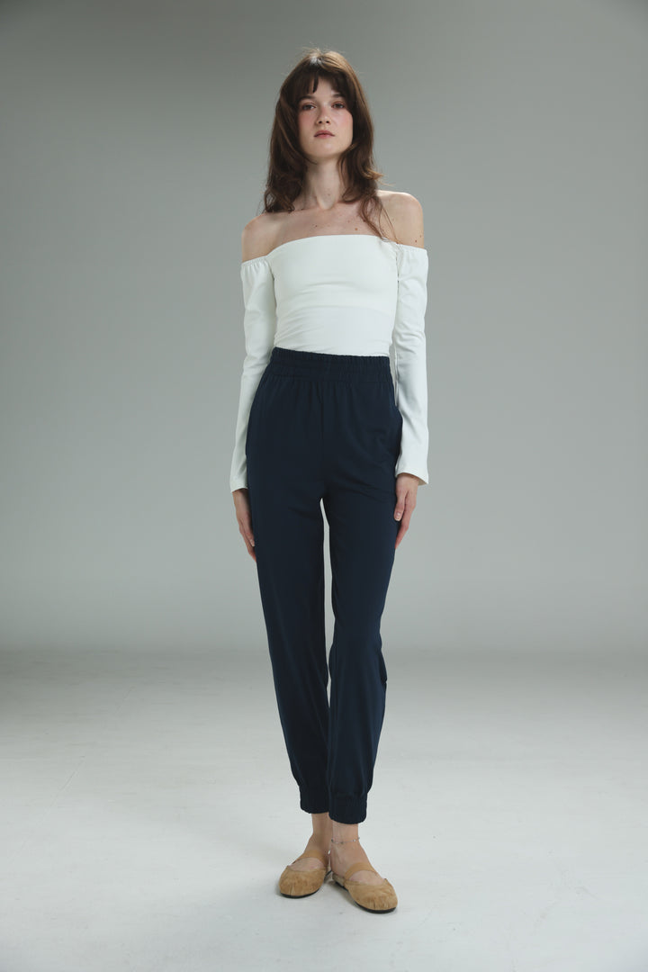 A white lycra off shoulder top with long sleeves shown from the front worn with dark navy high-waisted trousers