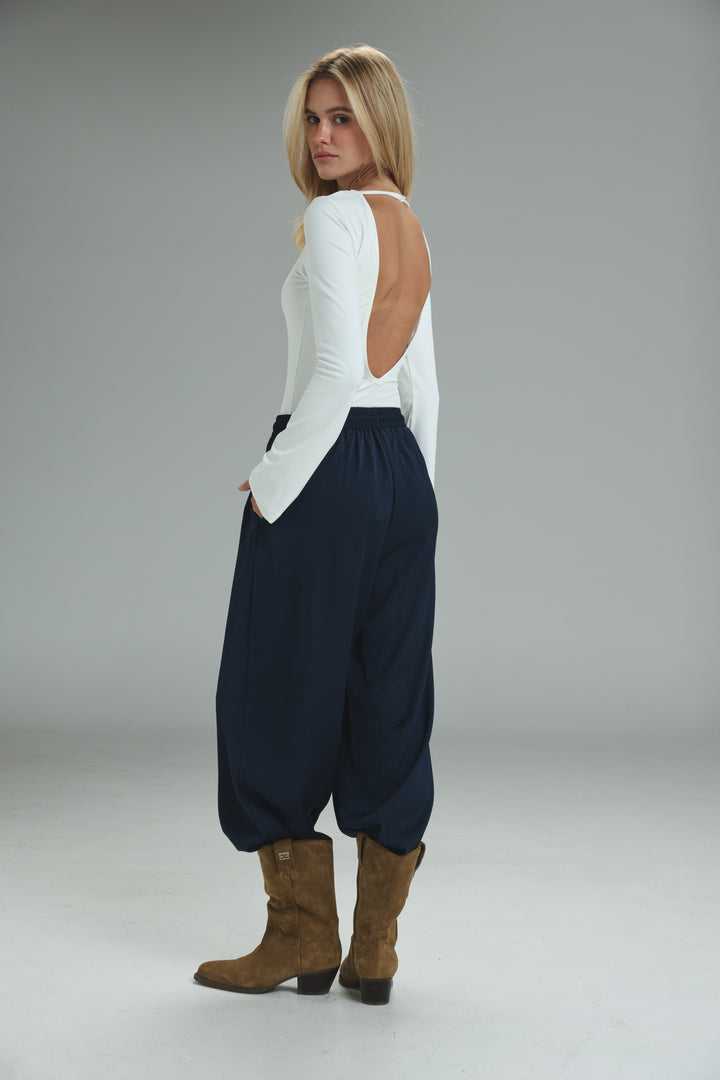 White long-sleeved top with back cutout paired with golden navy wide-leg pants shown from the side view