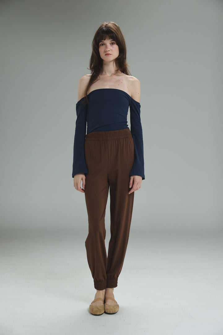 The lycra navy off shoulder top with long sleeves is shown from the front paired with brown high-waisted trousers