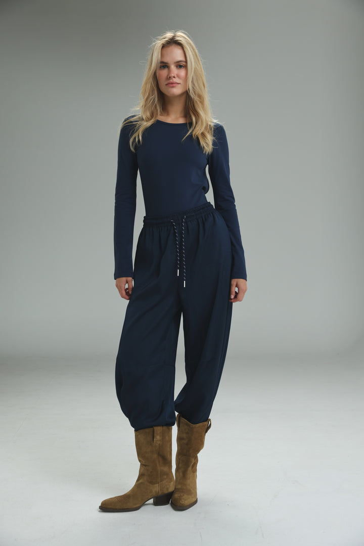 Navy blue long-sleeved jumpsuit with drawstring waist and tapered balloon-style pants shown from the front