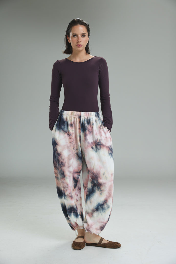The lycra purple open back bodysuit is shown with a front view paired with loose pink and navy tie-dye pants