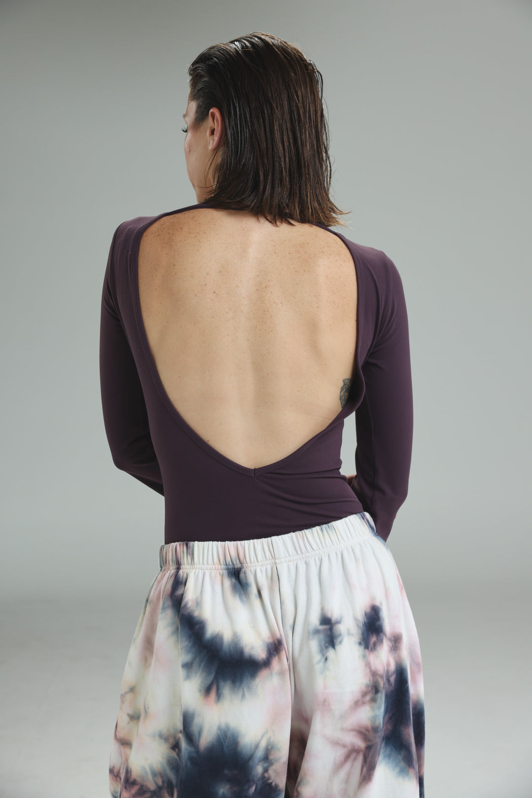 Lycra purple long-sleeved bodysuit with a wide open back design shown from the back view