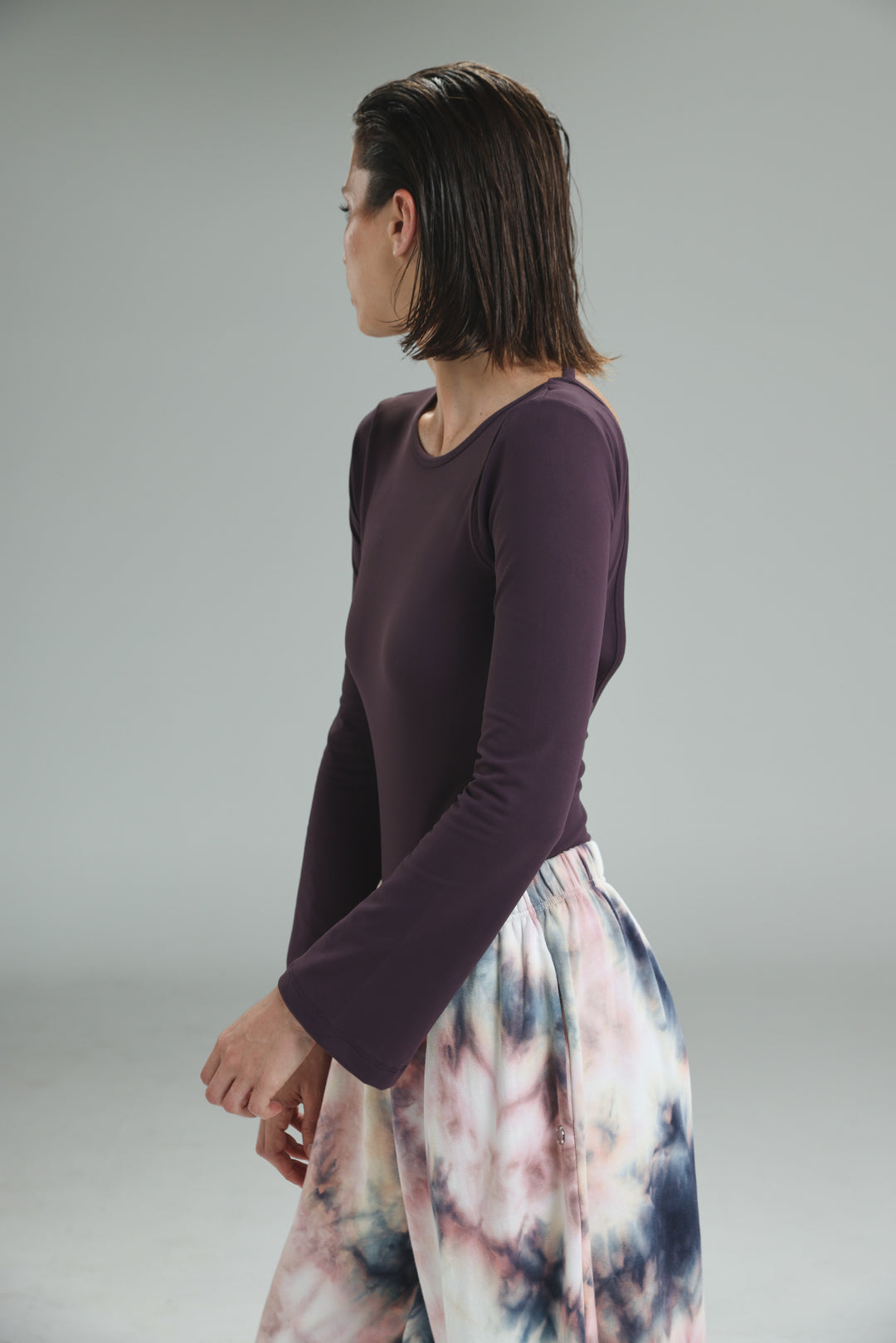 A woman wears a lycra purple open back bodysuit with long bell sleeves and a rounded neckline shown from the front