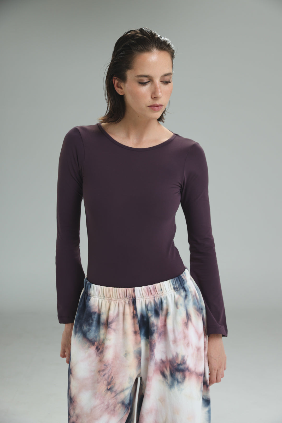 A front view of a lycra purple open back bodysuit with long sleeves and a round neckline