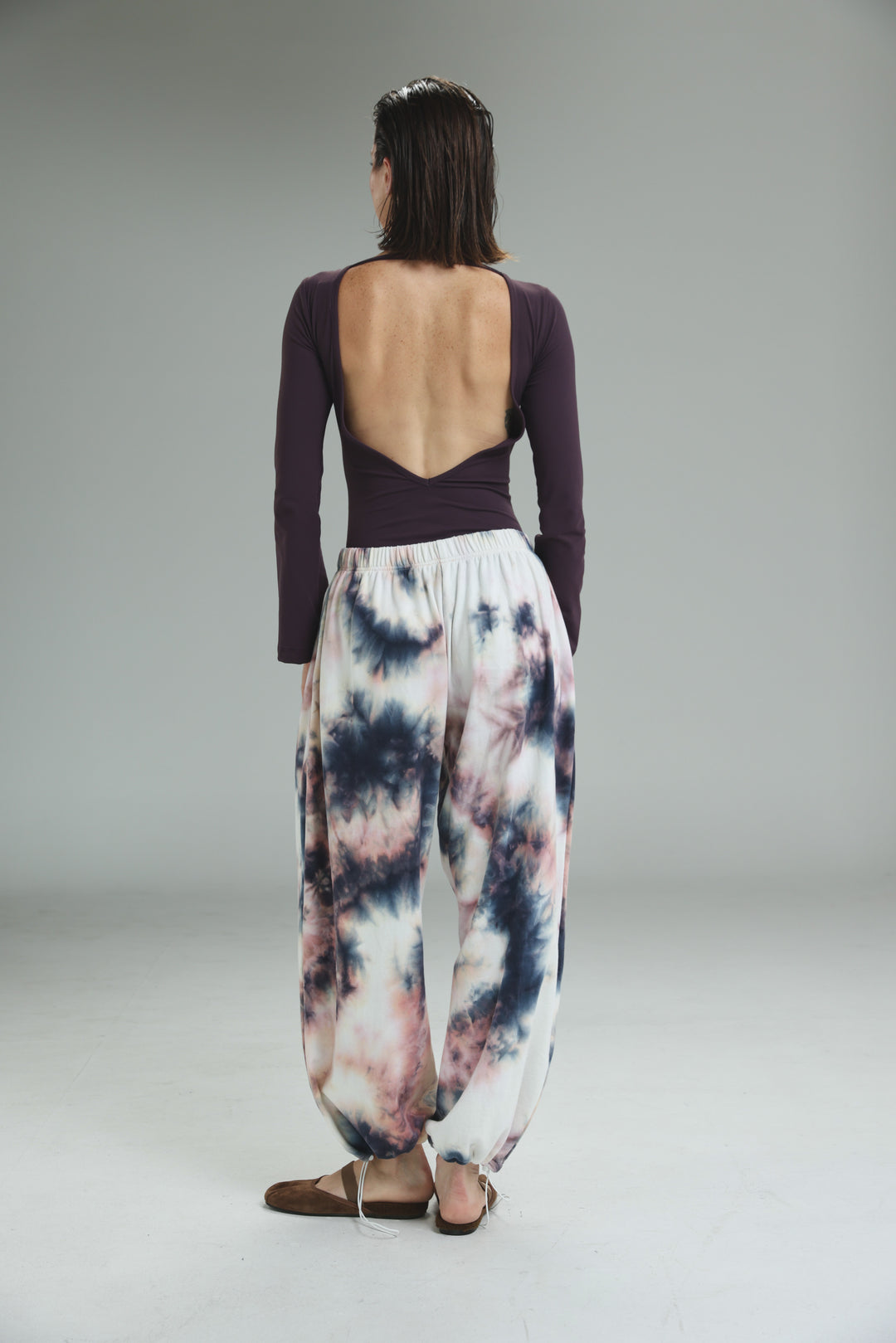 Lycra purple open back bodysuit shown with loose-fitting white tie-dye harem pants featuring black and pink patterns
