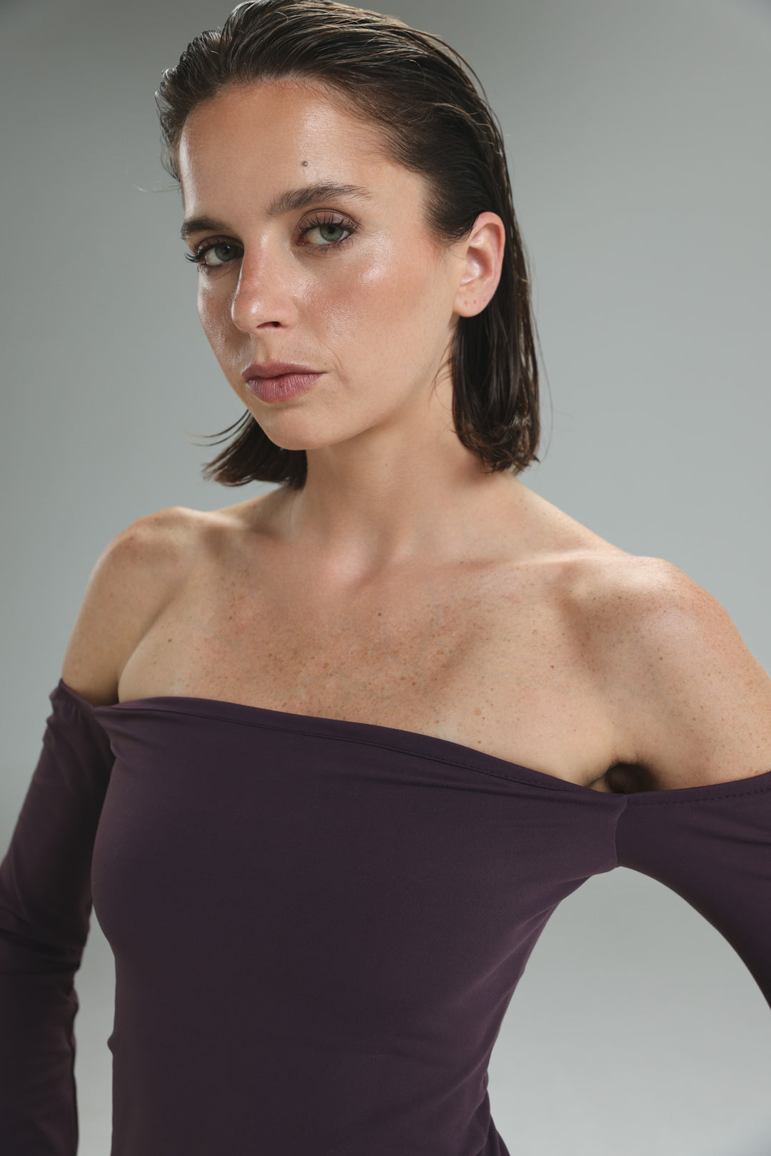 A woman wearing a deep purple lycra off shoulder top with long sleeves and a fitted silhouette from the front
