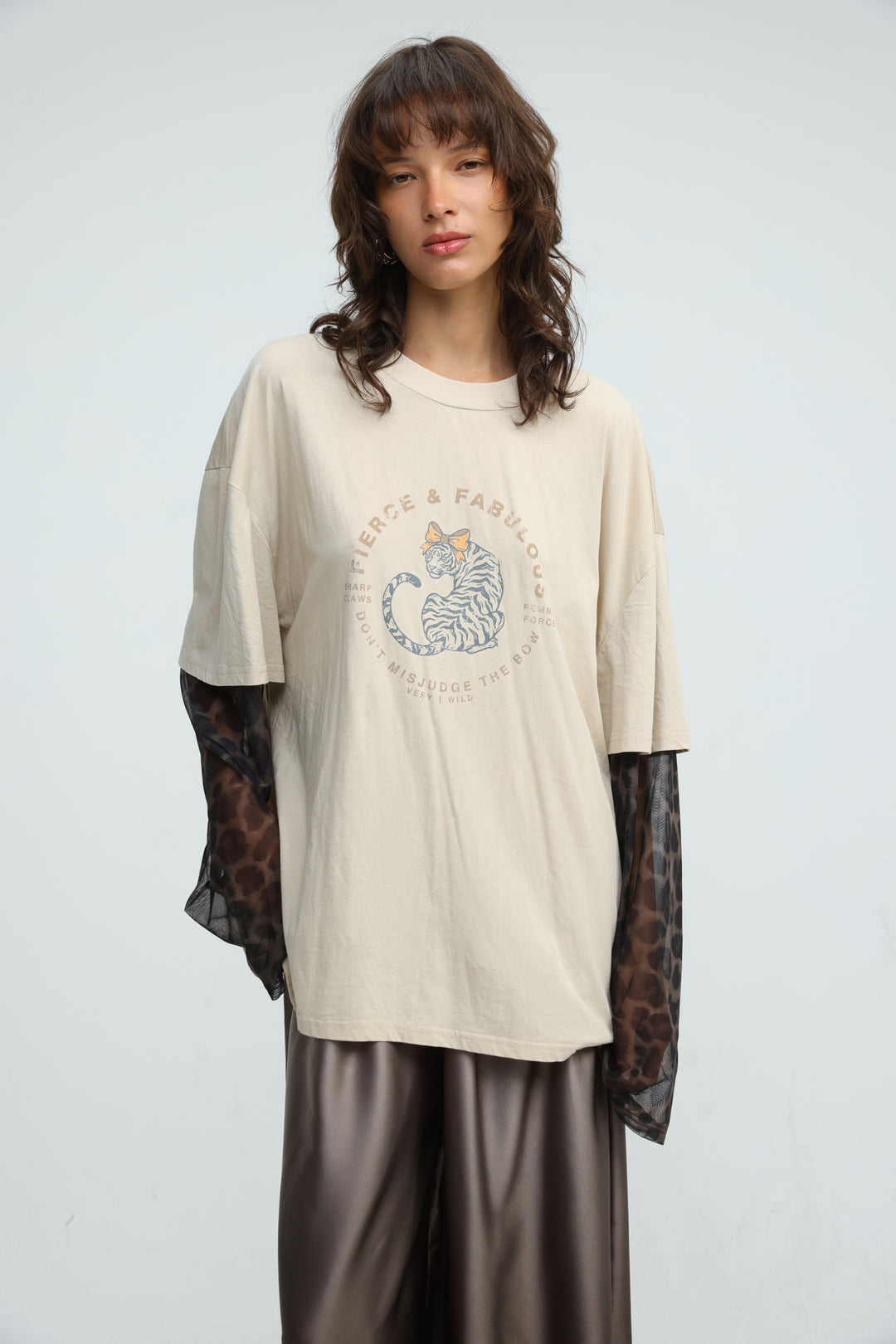 Beige oversized t-shirt with circular striped cat graphic and fierce and fabulous text layered over leopard mesh long sleeves