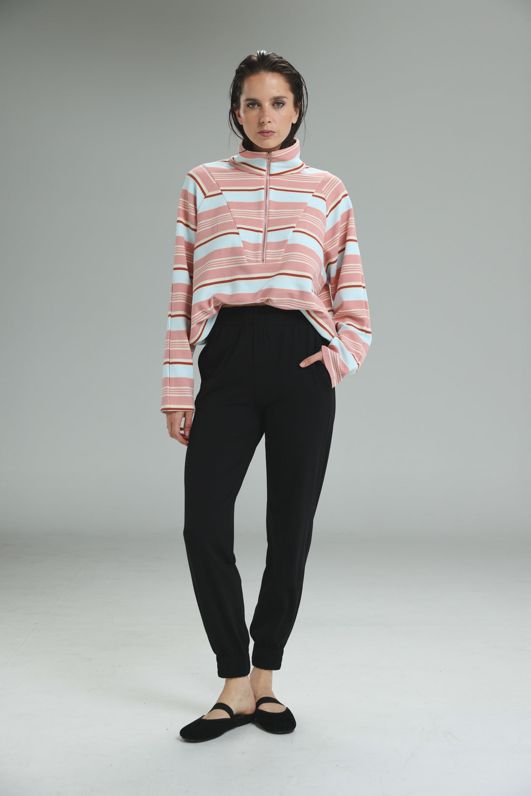 Bestie black joggers paired with a pink and light blue striped half zip sweater with ribbed collar shown from the front