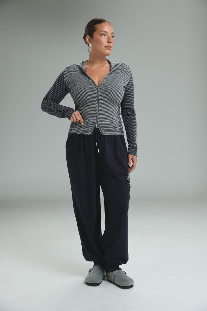A woman wearing a zip up brown stripes hoodie with long sleeves in a front view paired with dark navy sweatpants