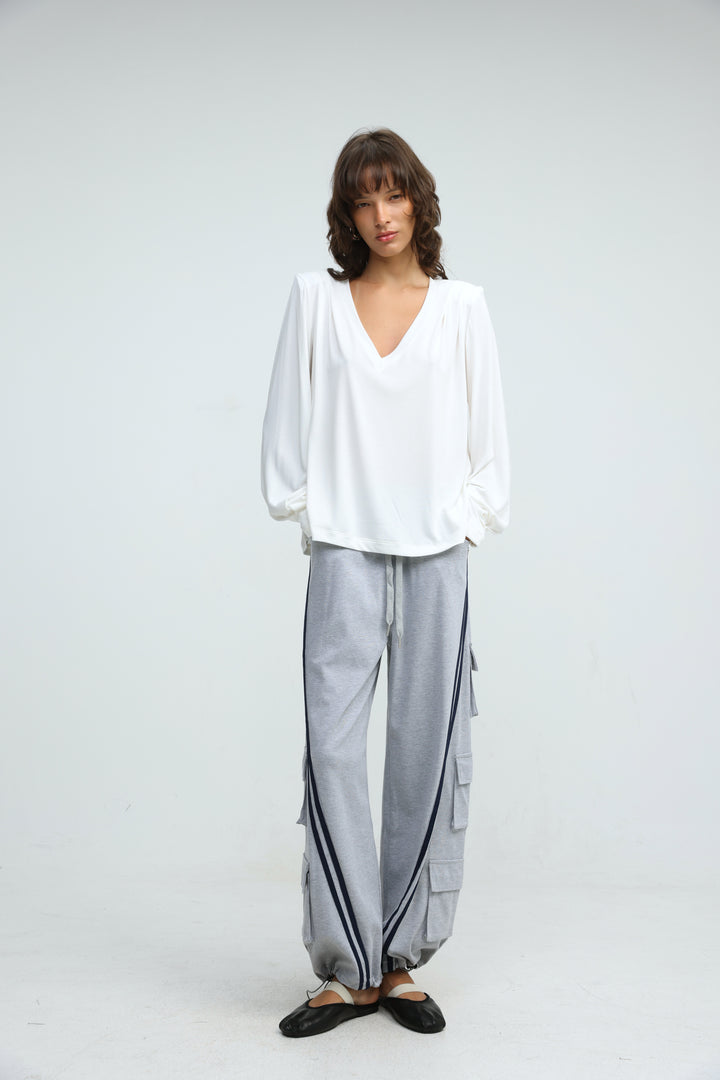 White v-neck blouse with loose flowing sleeves and relaxed fit paired with port grey joggers in front view