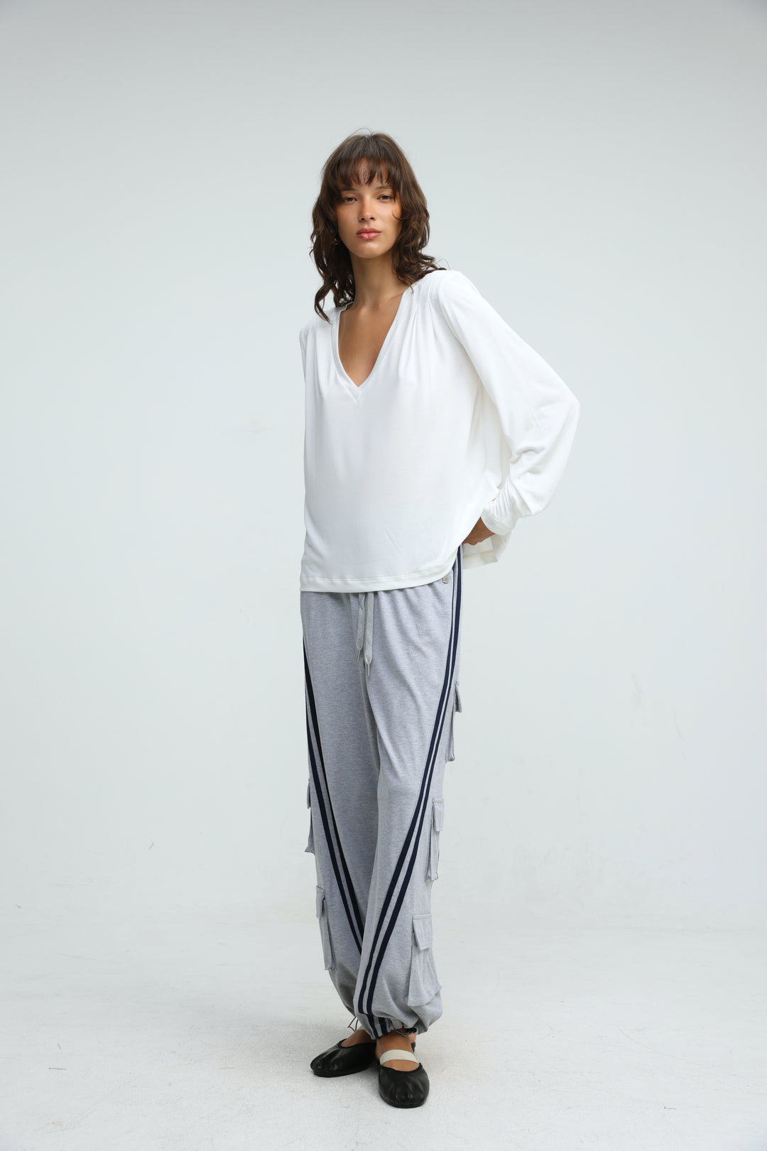 A front view of port grey joggers in light gray with black side stripes paired with a white loose v neck long sleeve top