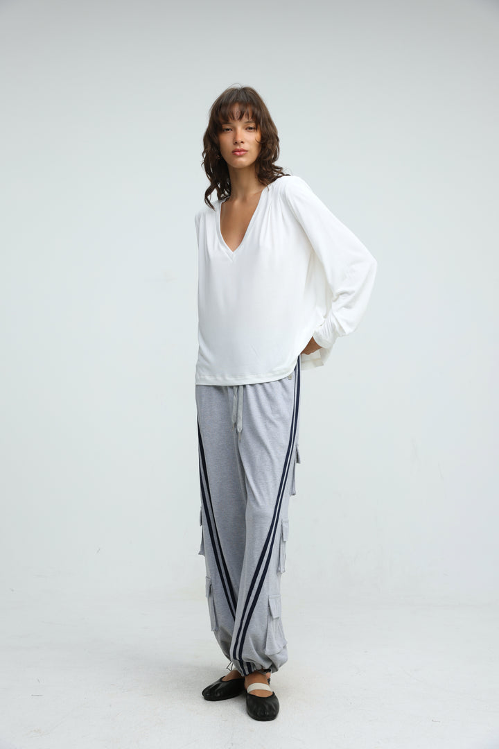 A front view of port grey joggers in light gray with black side stripes paired with a white loose v neck long sleeve top