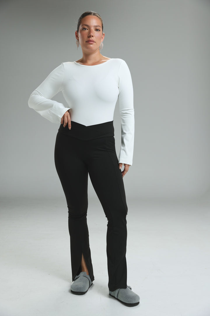 A woman wears front slit black leggings with a side slit paired with a white long-sleeved top with a boat neckline