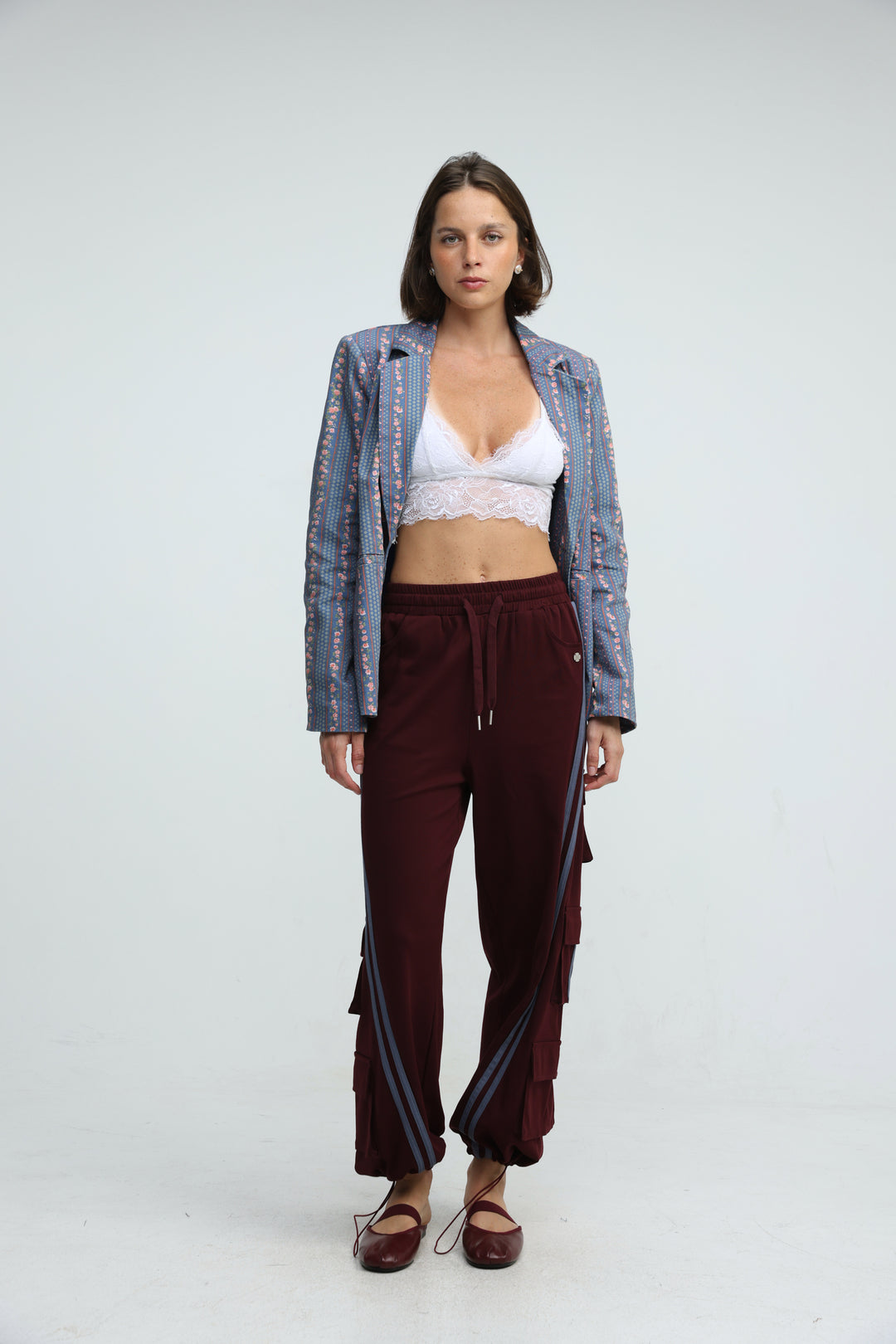 Woman wearing port wine joggers with side stripes shown from the front paired with a white lace crop top and blue sequined blazer