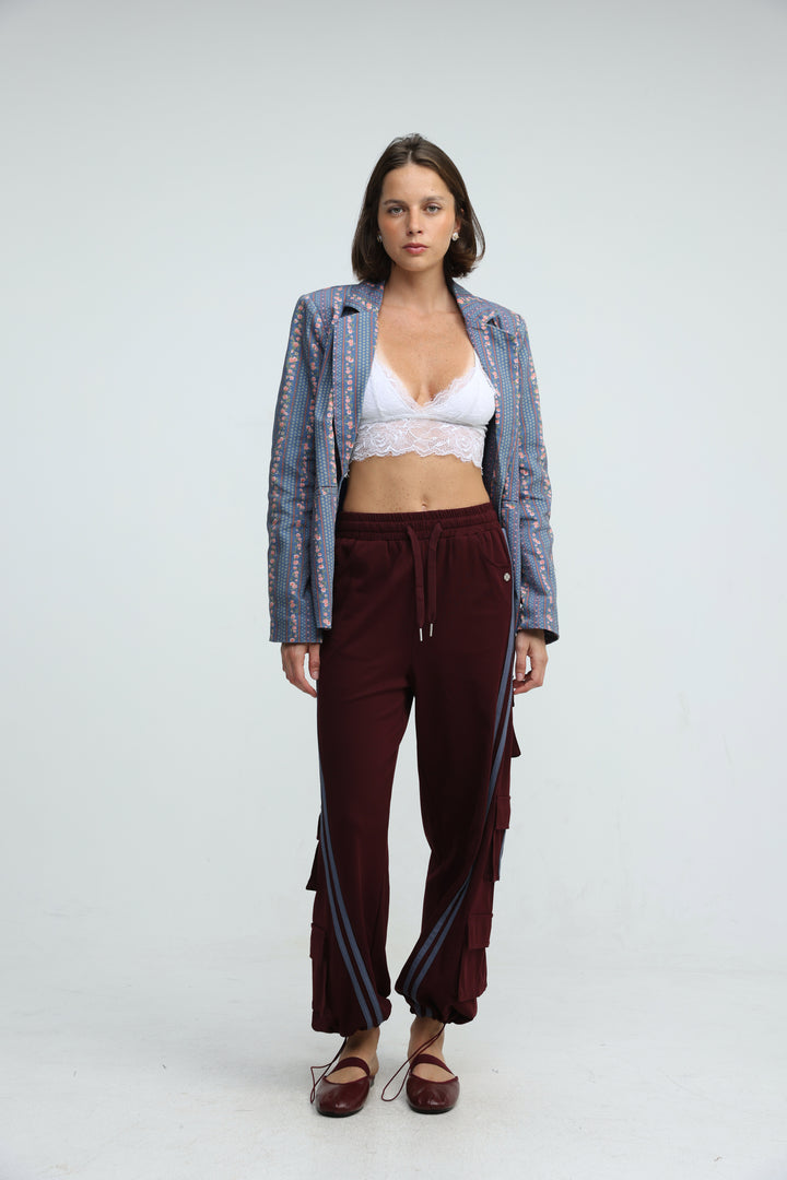 Woman wearing port wine joggers with side stripes shown from the front paired with a white lace crop top and blue sequined blazer