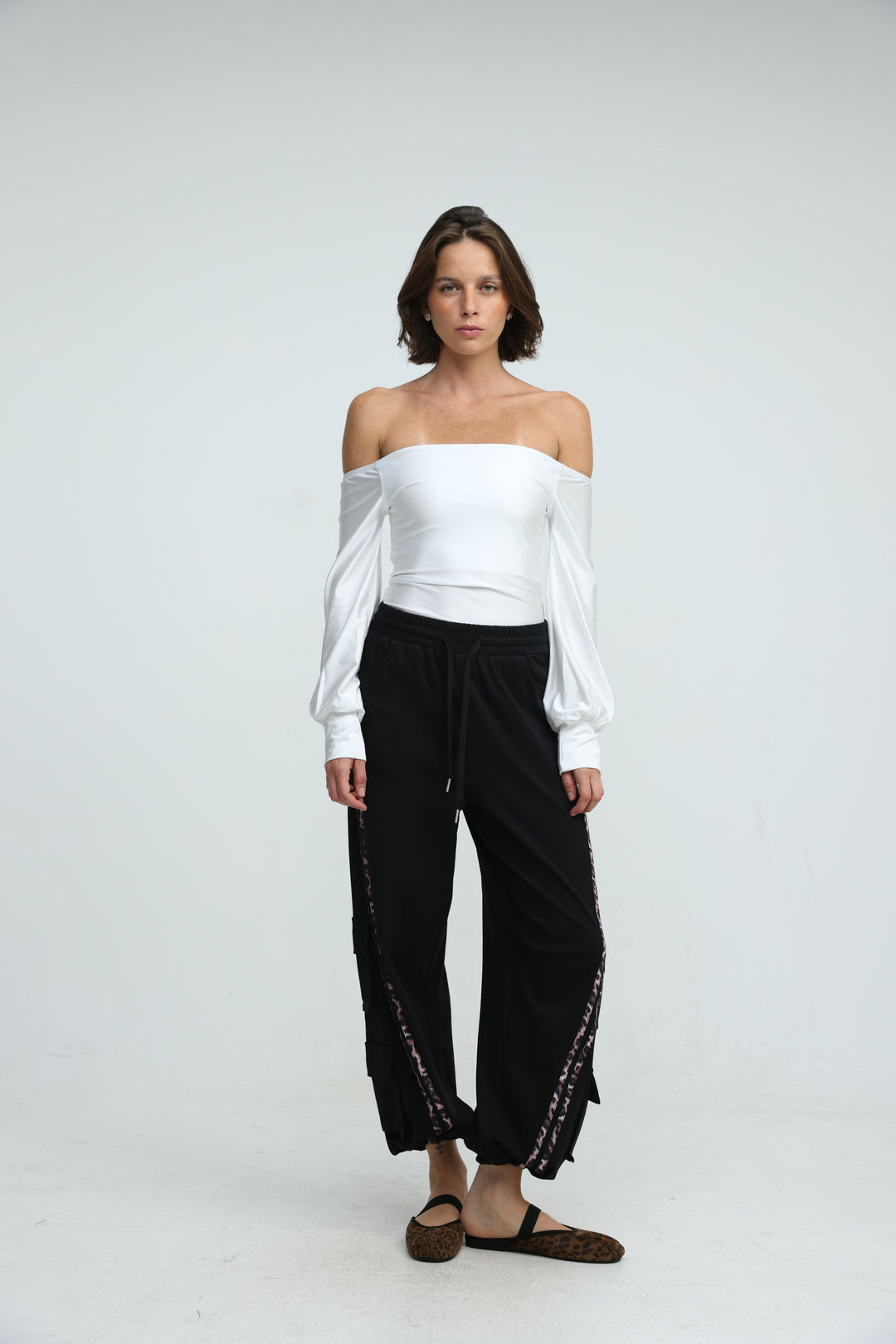 White off-the-shoulder blouse with long puffed sleeves and gathered waistband paired with black joggers front view