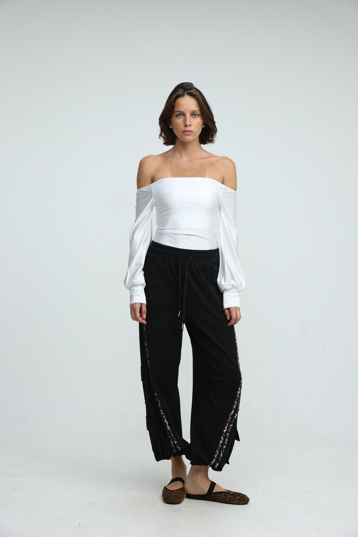 White off-the-shoulder blouse with long puffed sleeves and gathered waistband paired with black joggers front view