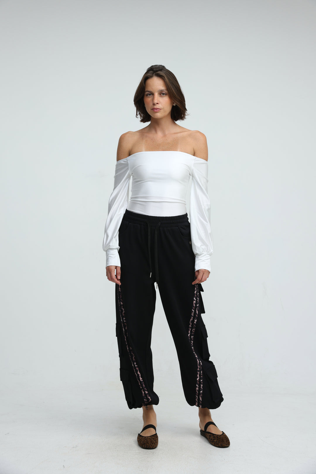 White off-the-shoulder blouse with long sleeves and cinched waist paired with black joggers front view