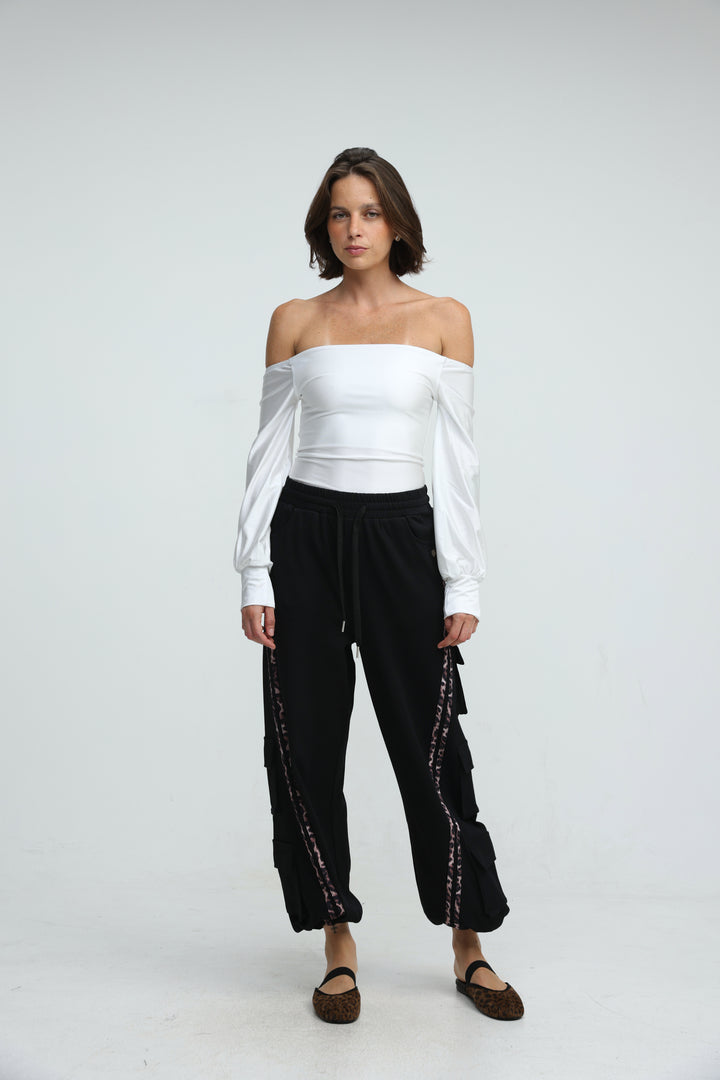 White off-the-shoulder blouse with long sleeves and cinched waist paired with black joggers front view