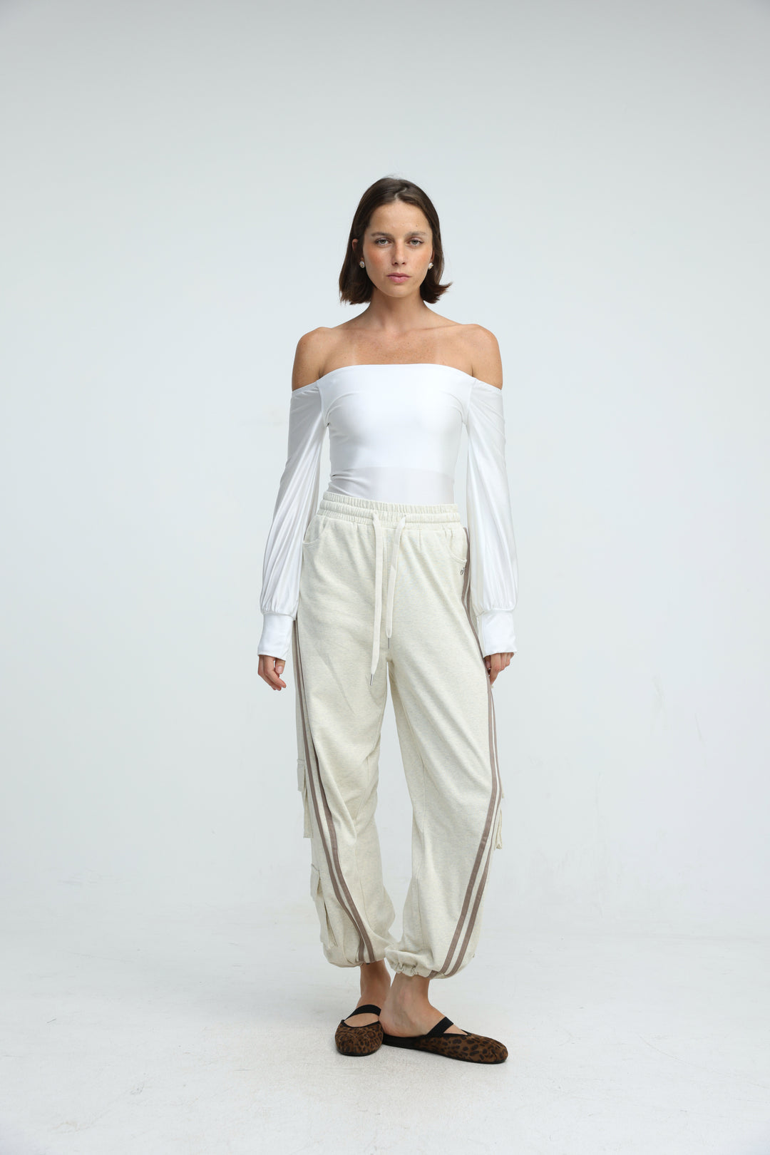 Front view of cream-colored drawstring joggers with side stripes paired with a white off-the-shoulder  top with long sleeves