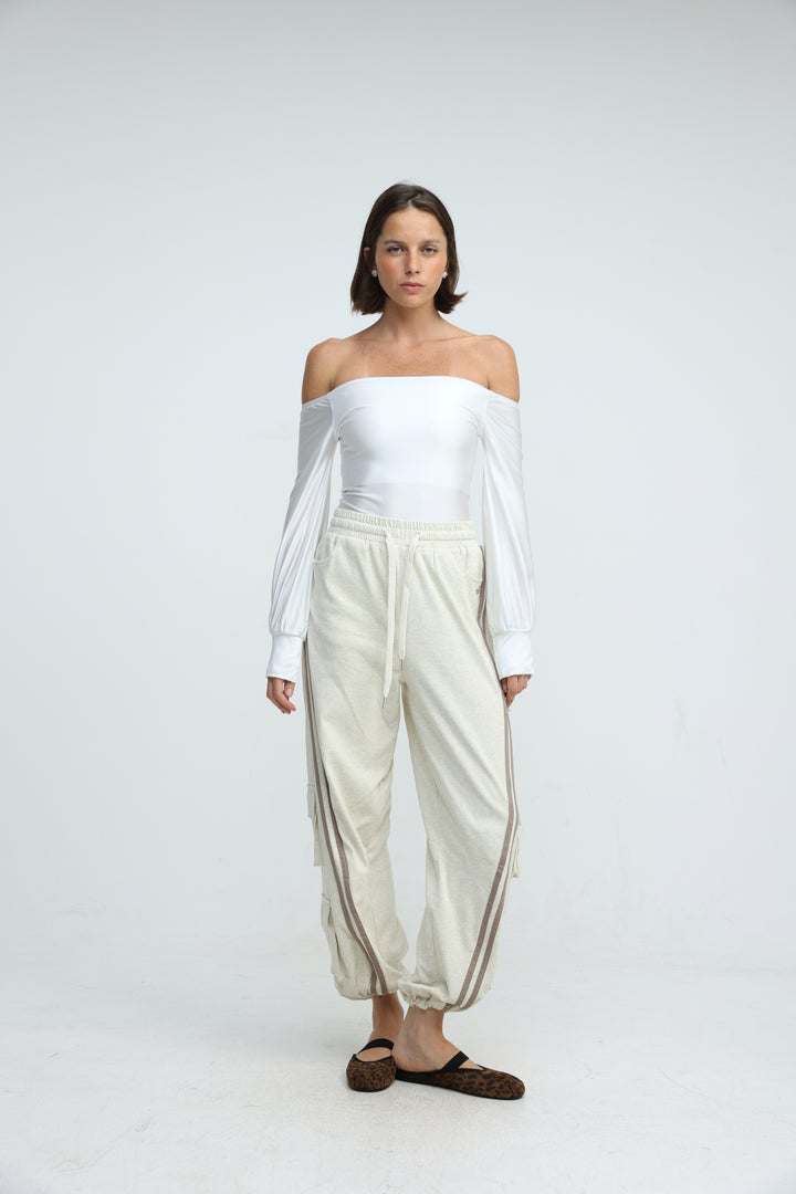 Front view of cream-colored drawstring joggers with side stripes paired with a white off-the-shoulder  top with long sleeves