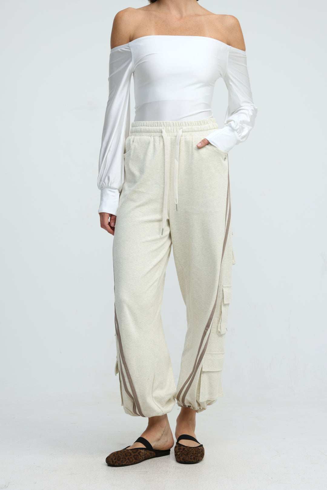 Cream-colored cargo jogger pants with gray striped side panels and multiple front and thigh pockets front view