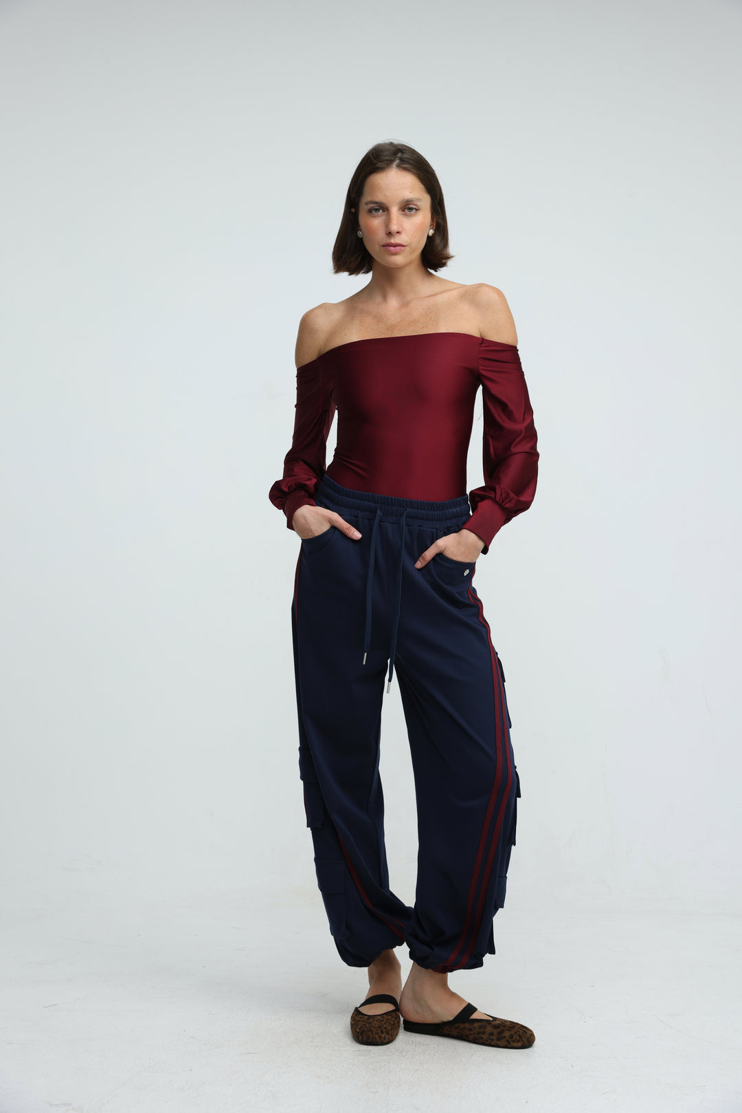 A front view of navy cargo joggers with maroon side stripes paired with a  burgundy off the shoulder top
