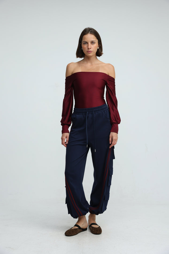 A woman wears port navy joggers with side panels and a burgundy off-the-shoulder long sleeve top, front view