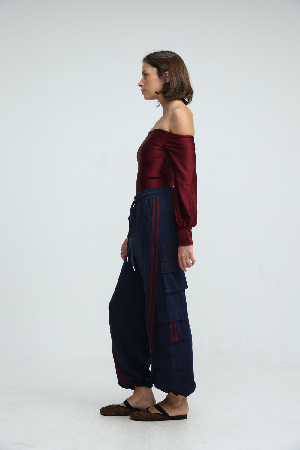 A front view of port navy joggers in navy blue with vertical red stripes and multiple cargo pockets paired with a burgundy off-shoulder top