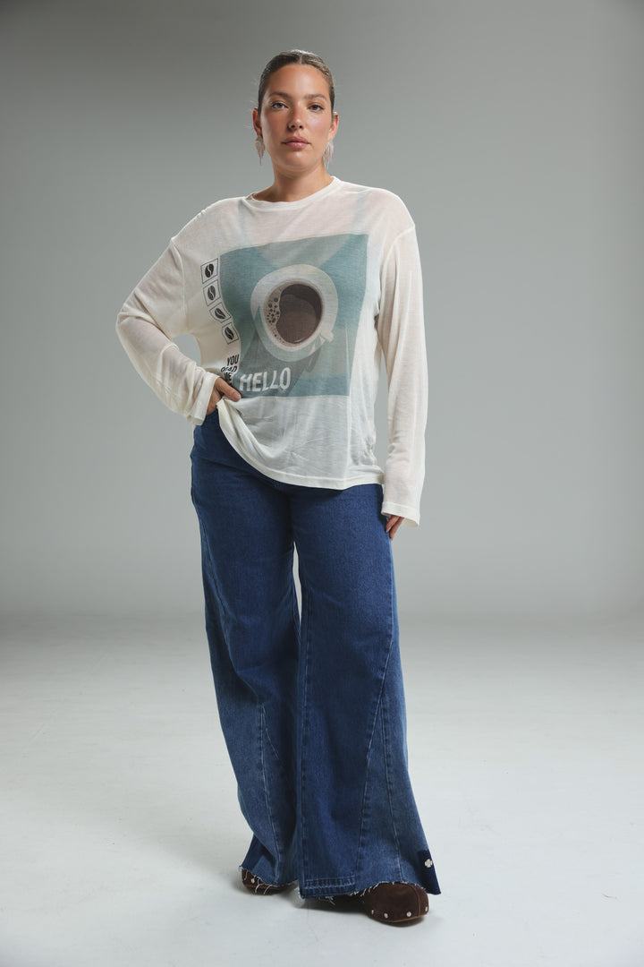 White long-sleeved Hello Coffee Cream shirt with teal circular design and hello text, front view over blue wide-leg pants