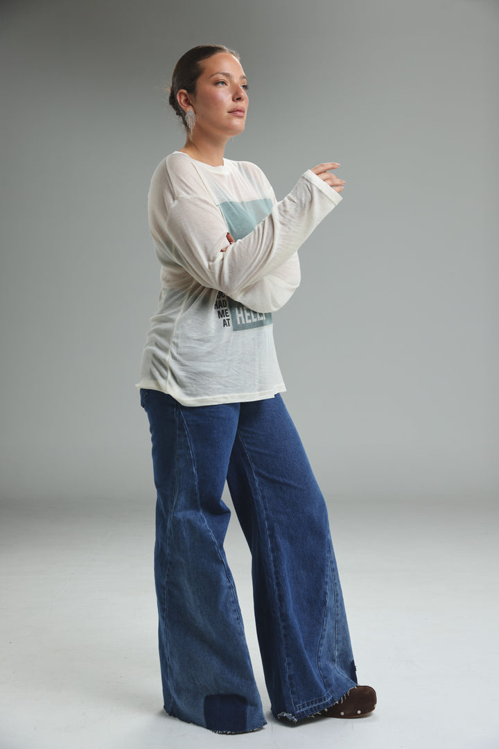 A woman wearing a white Hello Coffee Cream long-sleeved graphic tee with teal and black text paired with wide-leg denim pants