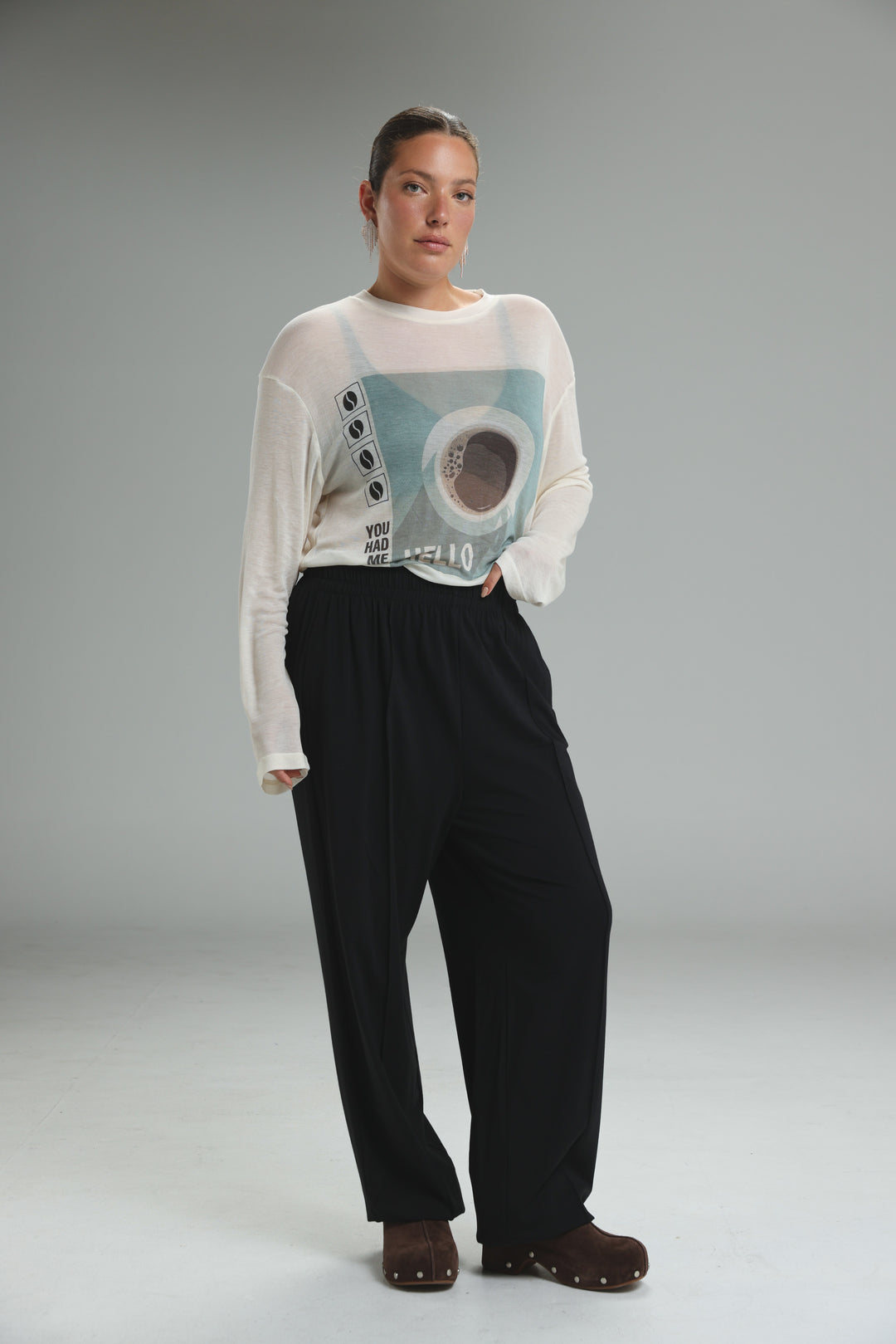 White sheer long-sleeved hello coffee cream shirt with coffee cup graphic worn over black wide-leg pants front view