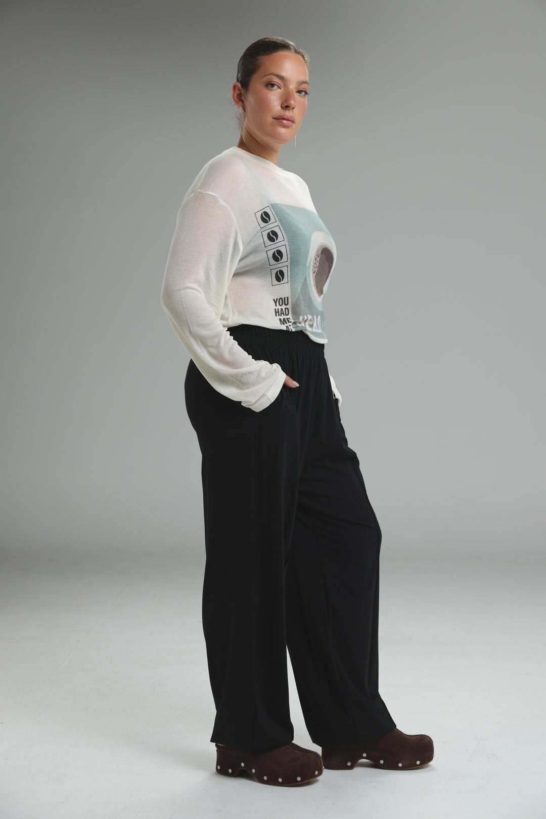 White long-sleeved top with graphic print and sheer overlay paired with black joggers shown from front view