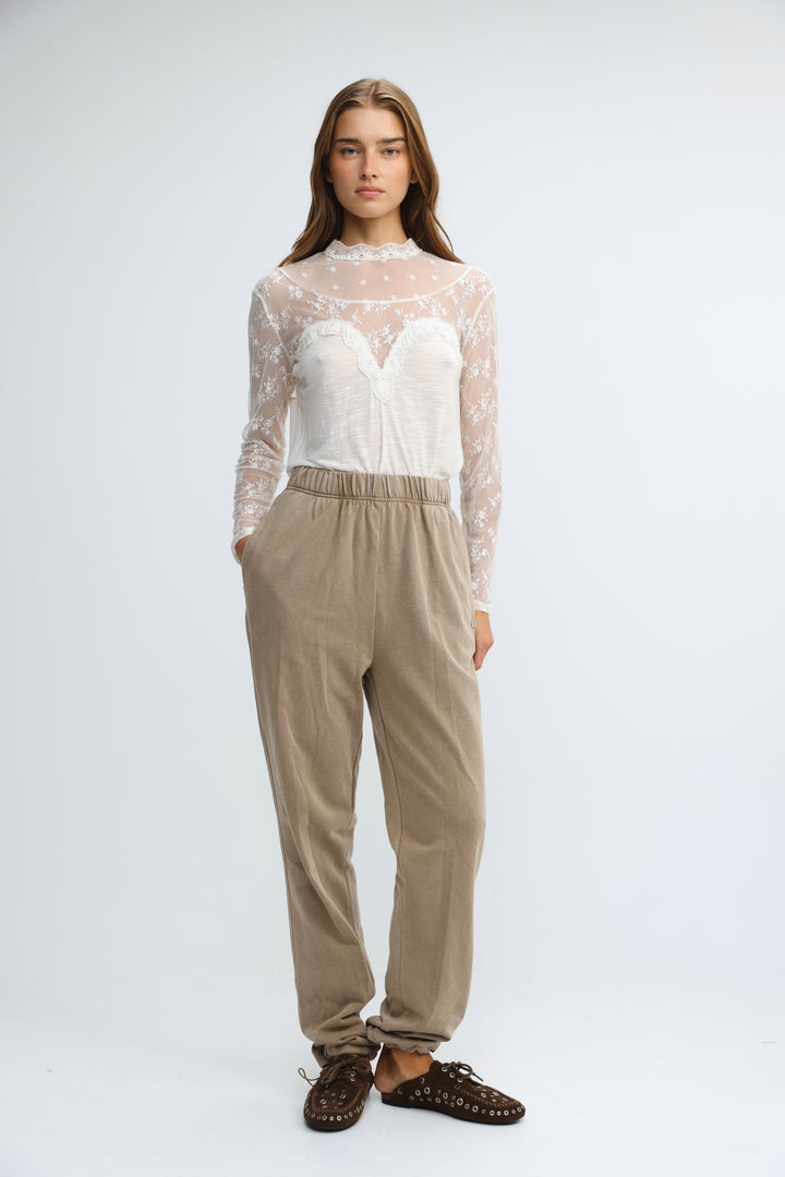 A woman wearing camel joggers paired with a sheer long-sleeved lace top over a white corset-style bodice front view
