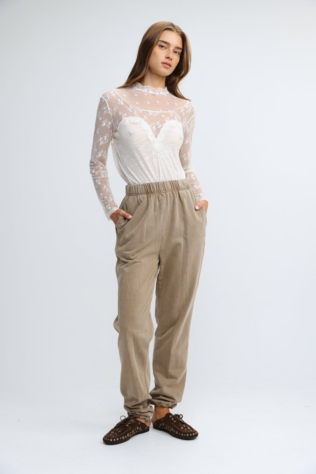 A front view of camel joggers with an elastic waist paired with a sheer lace long-sleeved white bodice top