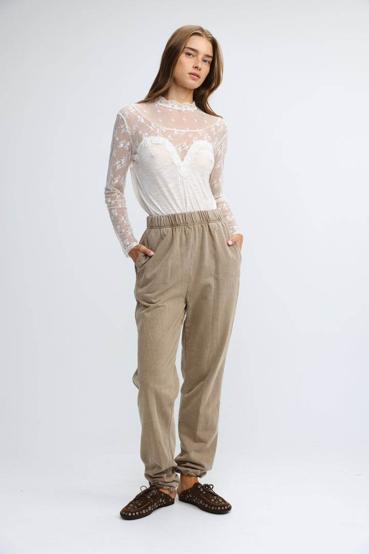 A front view of camel joggers with an elastic waist paired with a sheer lace long-sleeved white bodice top