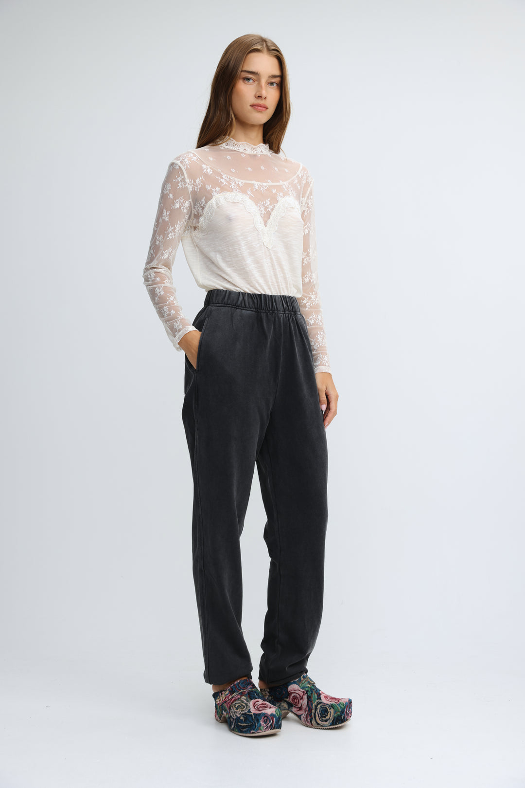 A woman wearing black  zone joggers shown from the front with a sheer lace floral top and patterned platform shoes
