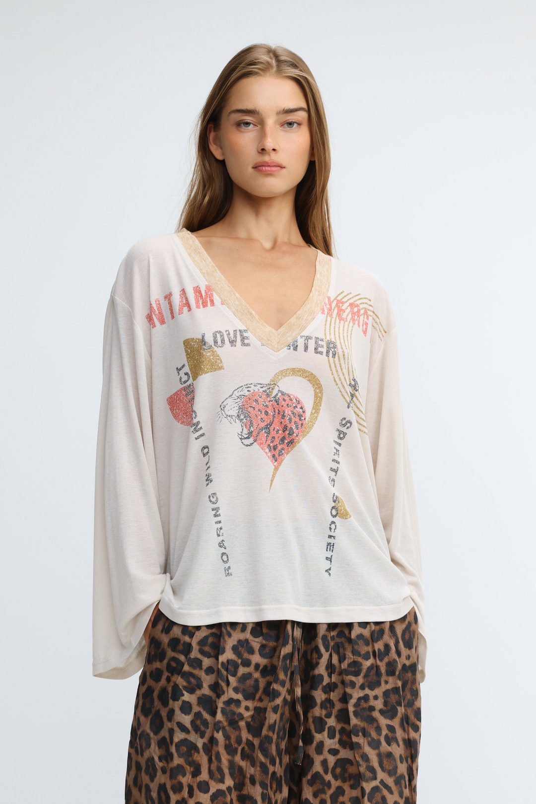 Off-white loose-fitting long-sleeved V-neck top with a gold foil tiger heart graphic and love and #roaring spirit society text