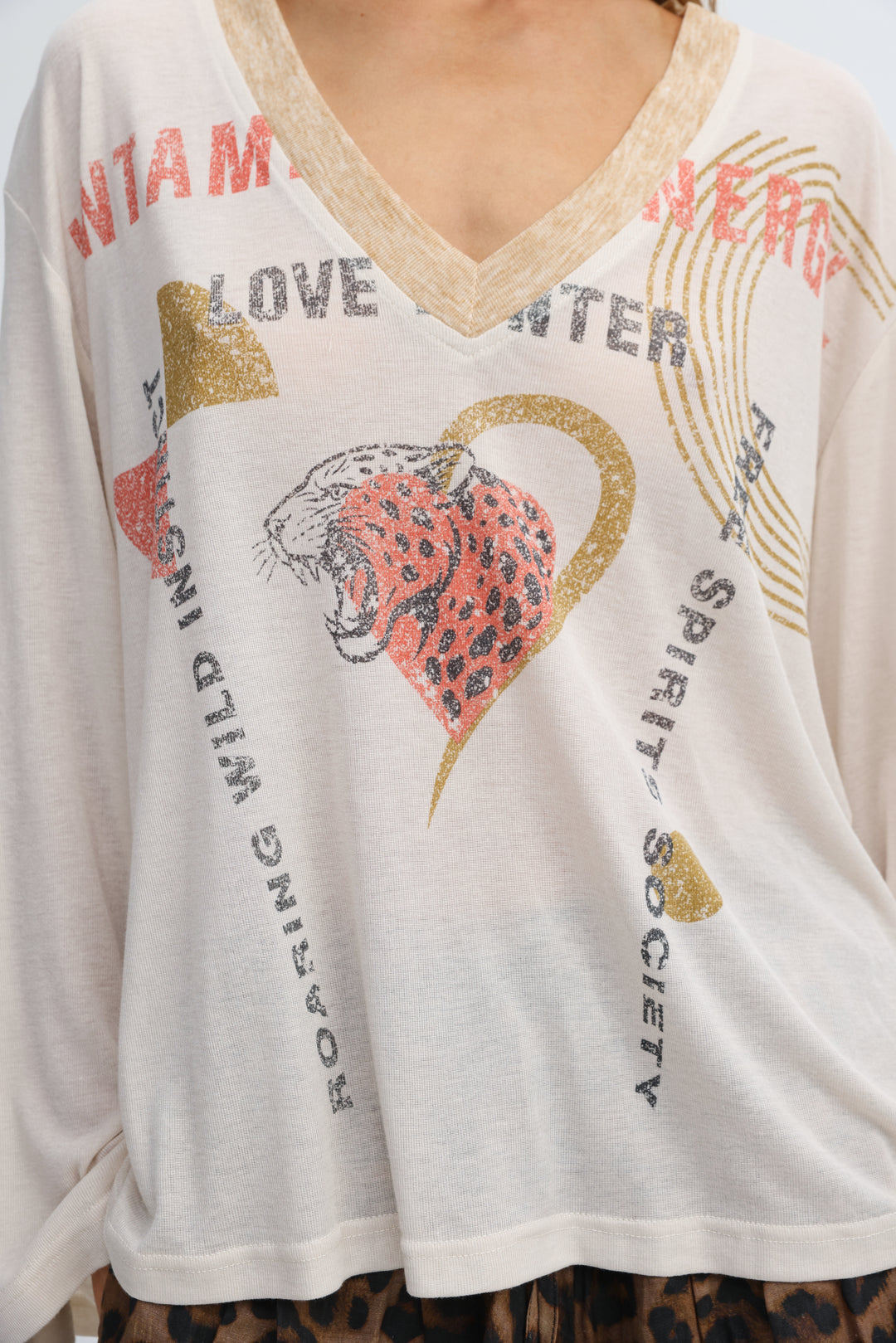 Cream-colored long-sleeved v-neck top with leopard print graphic inside a gold heart and glittery distressed text front view