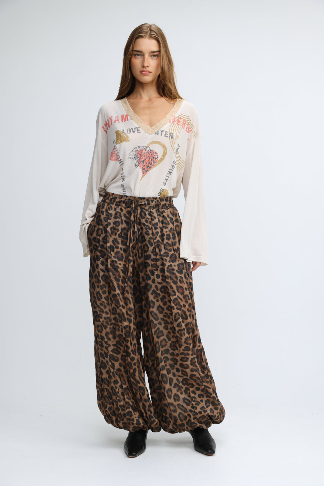 A woman wearing a cream-colored jungle cream V shirt with long sleeves and a V-neck paired with wide-leg leopard trousers