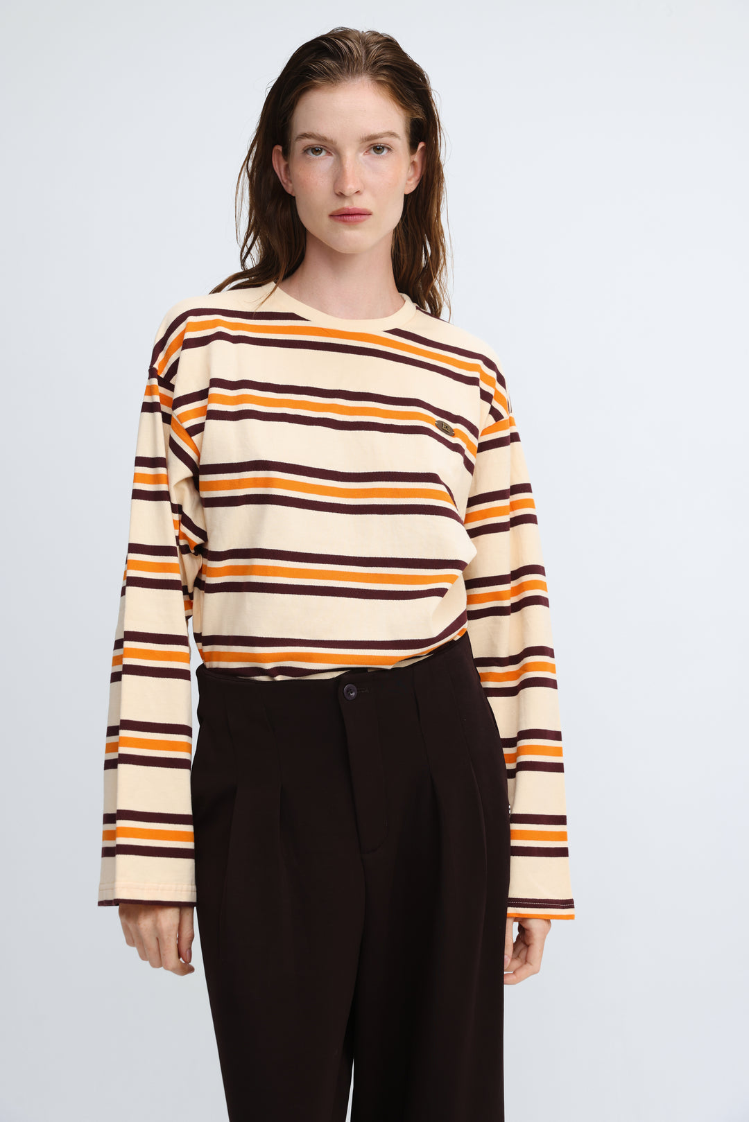 Cream-colored long-sleeved sweater with horizontal orange and dark brown stripes shown from the front