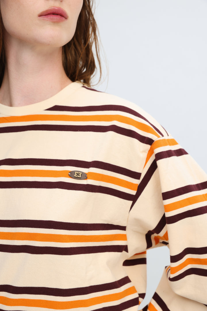 Cream-colored sweatshirt with bold orange and dark brown horizontal stripes and small metallic logo patch on front
