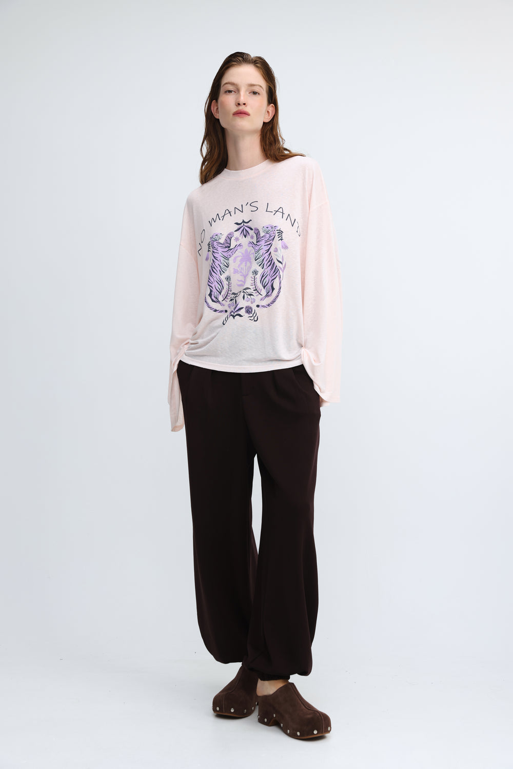A soft pink long-sleeved graphic tee with a purple and black embroidered design and no mans land text on front