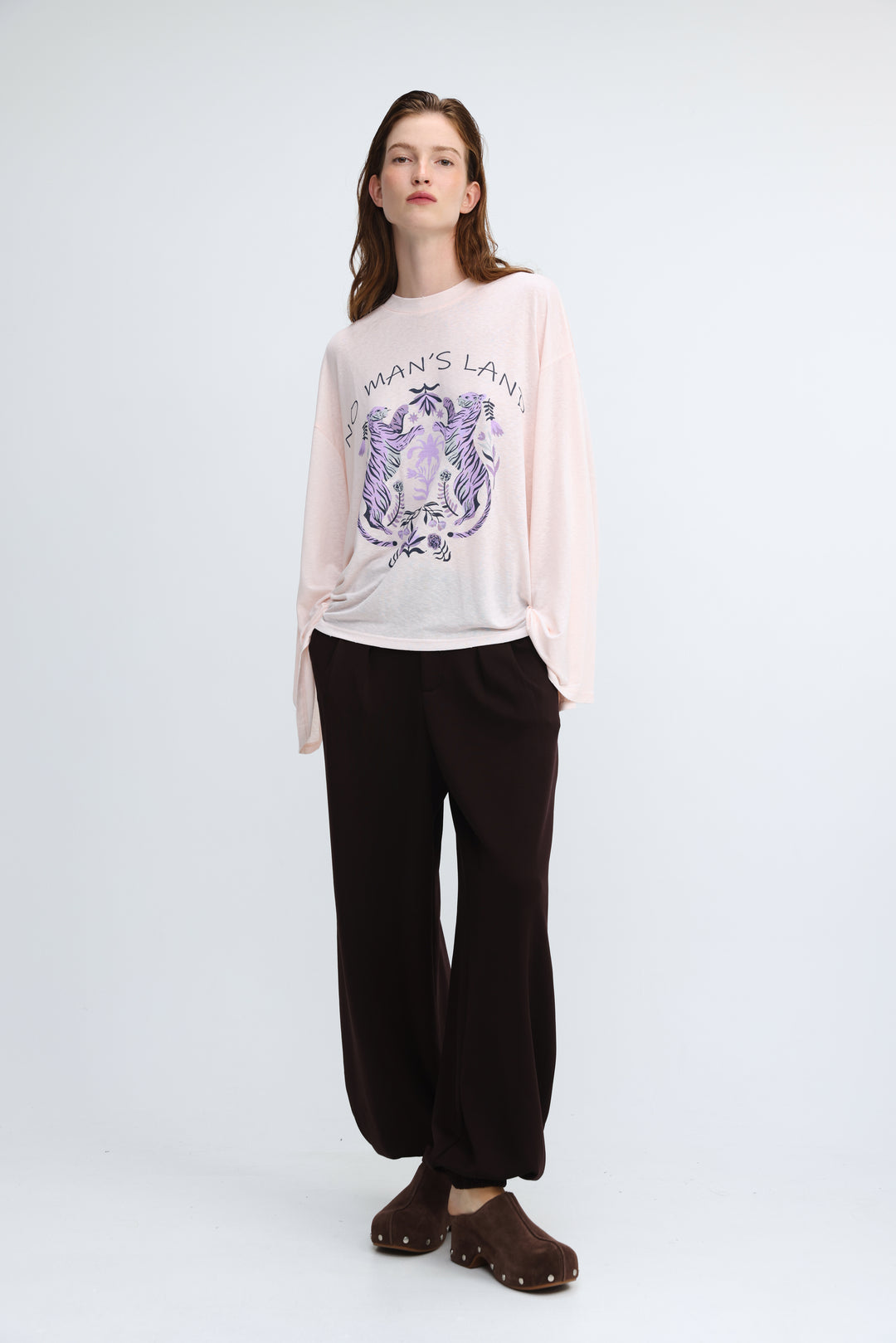 A soft pink long-sleeved graphic tee with a purple and black embroidered design and no mans land text on front