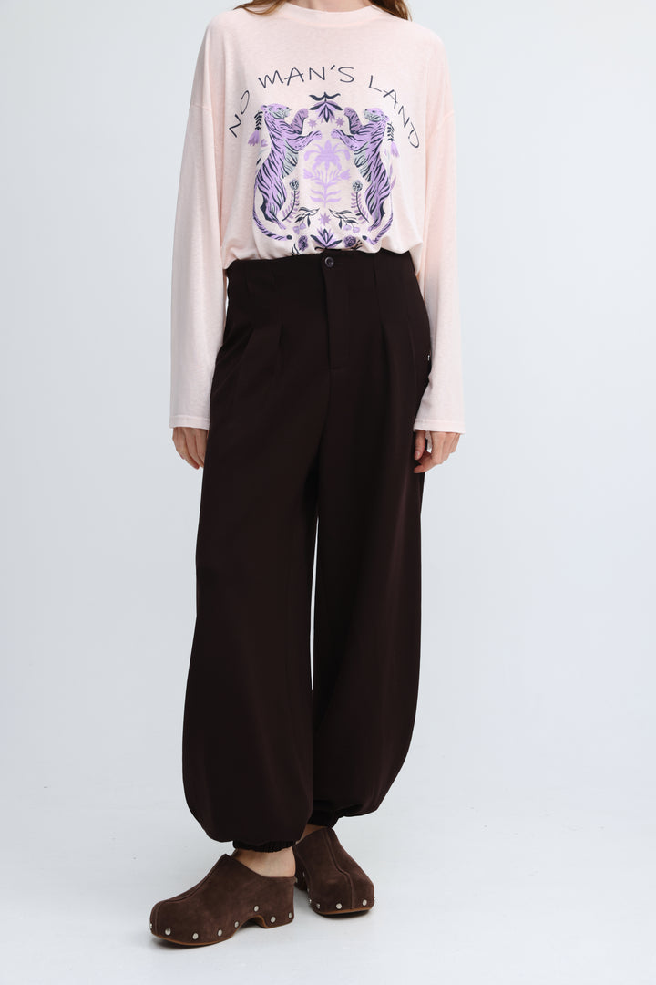 Pale pink long-sleeved top with purple and black no mans land graphic print in front view from everything brown bottoms