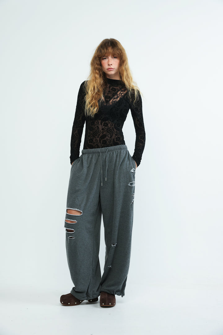 Dark grey loose-fitting joggers with distressed ripped details and drawstring waistband shown from the front