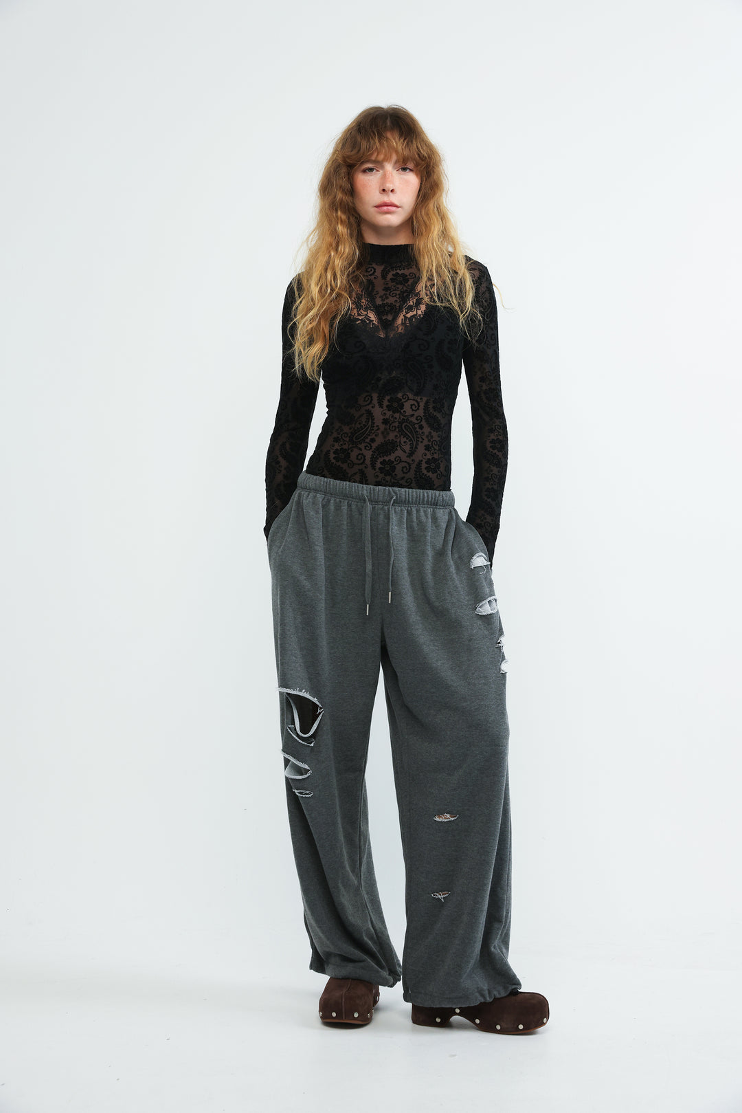 A pair of dark grey joggers with a drawstring waistband and distressed ripped details shown from the front