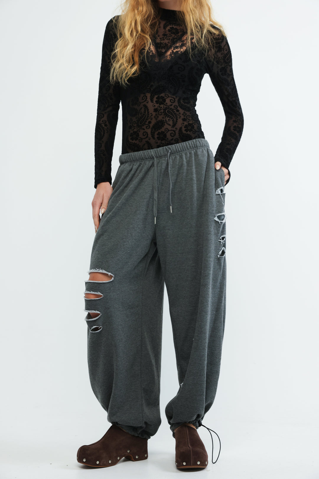Dark gray loose-fitting jogger pants with distressed rips and silver metal eyelets along the side seams front view